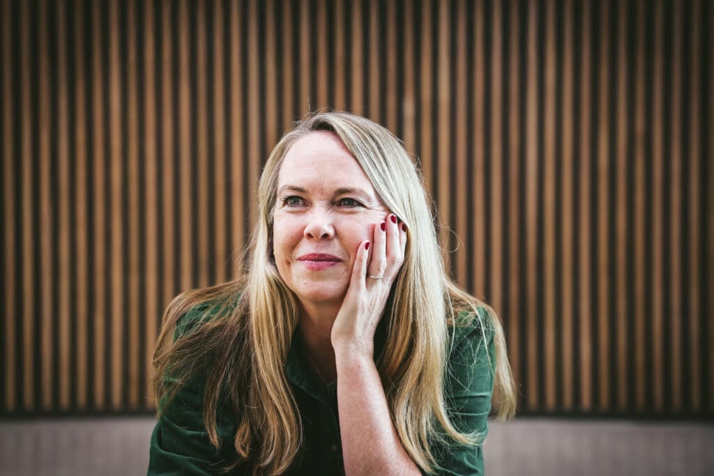 Melinda McDougall, smiling, wearing green dress, leaning her face in her palm