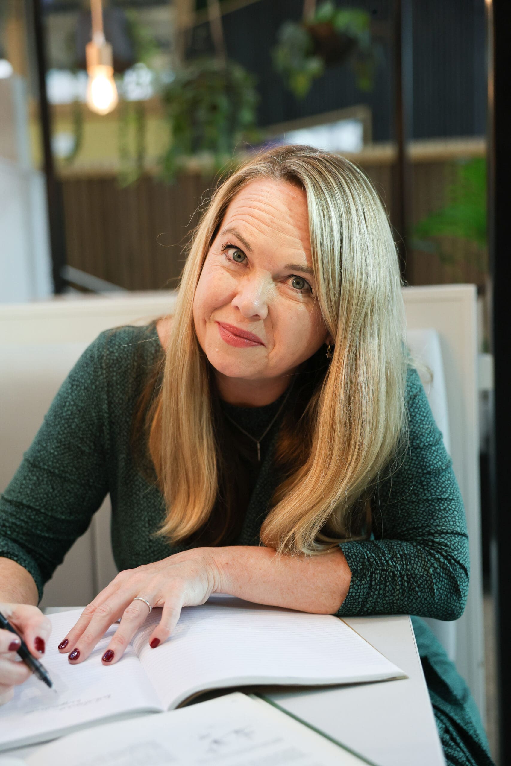 Melinda McDougall, writing in the notebook, smiling, wearing green dress