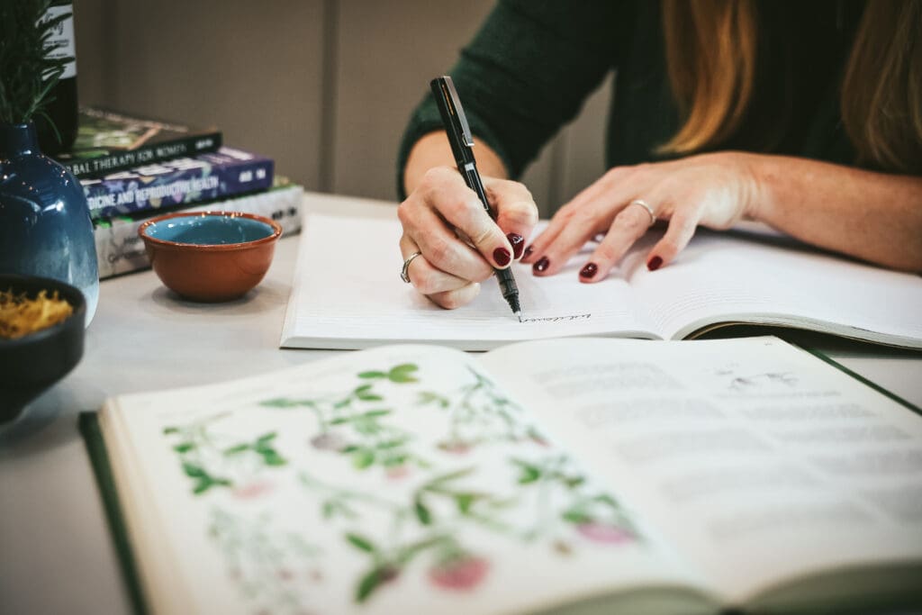 Melinda McDougall, writing in the notebook, herbal plants book open