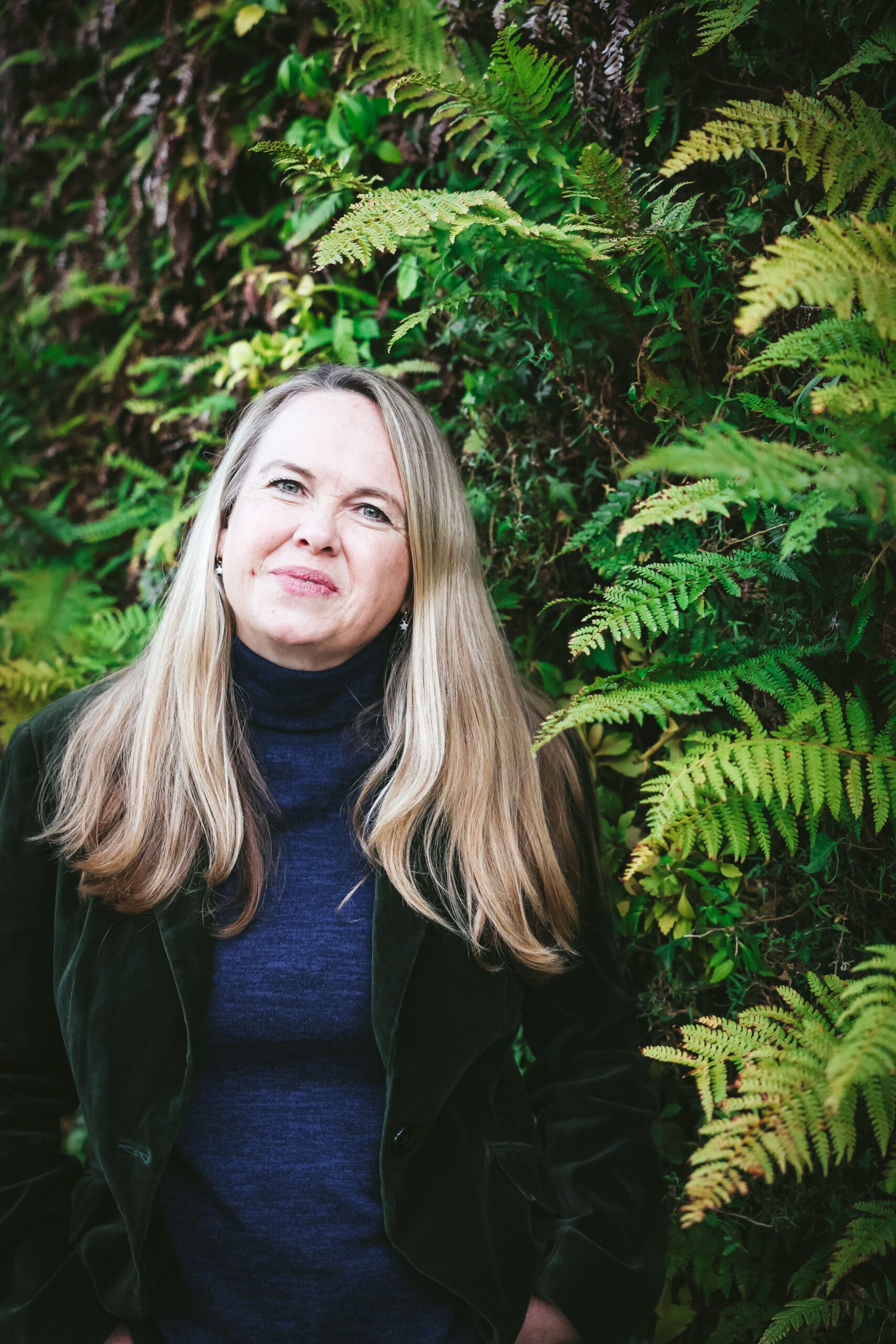 Melinda McDougall, with green leaves plant as background, wearing green coat and blue shir
