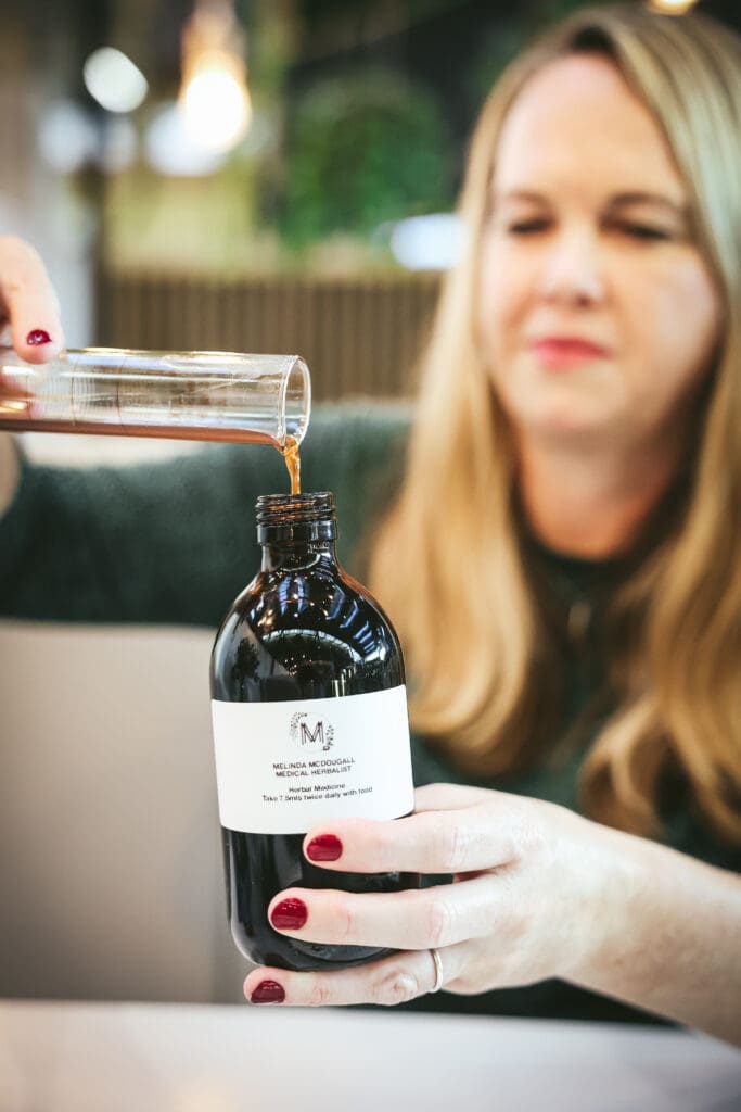 Melinda McDougall, pouring herbal liquid in the bottle using cylinder